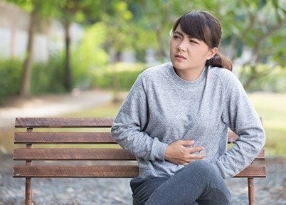 Woman sitting on bench, holding her stomach